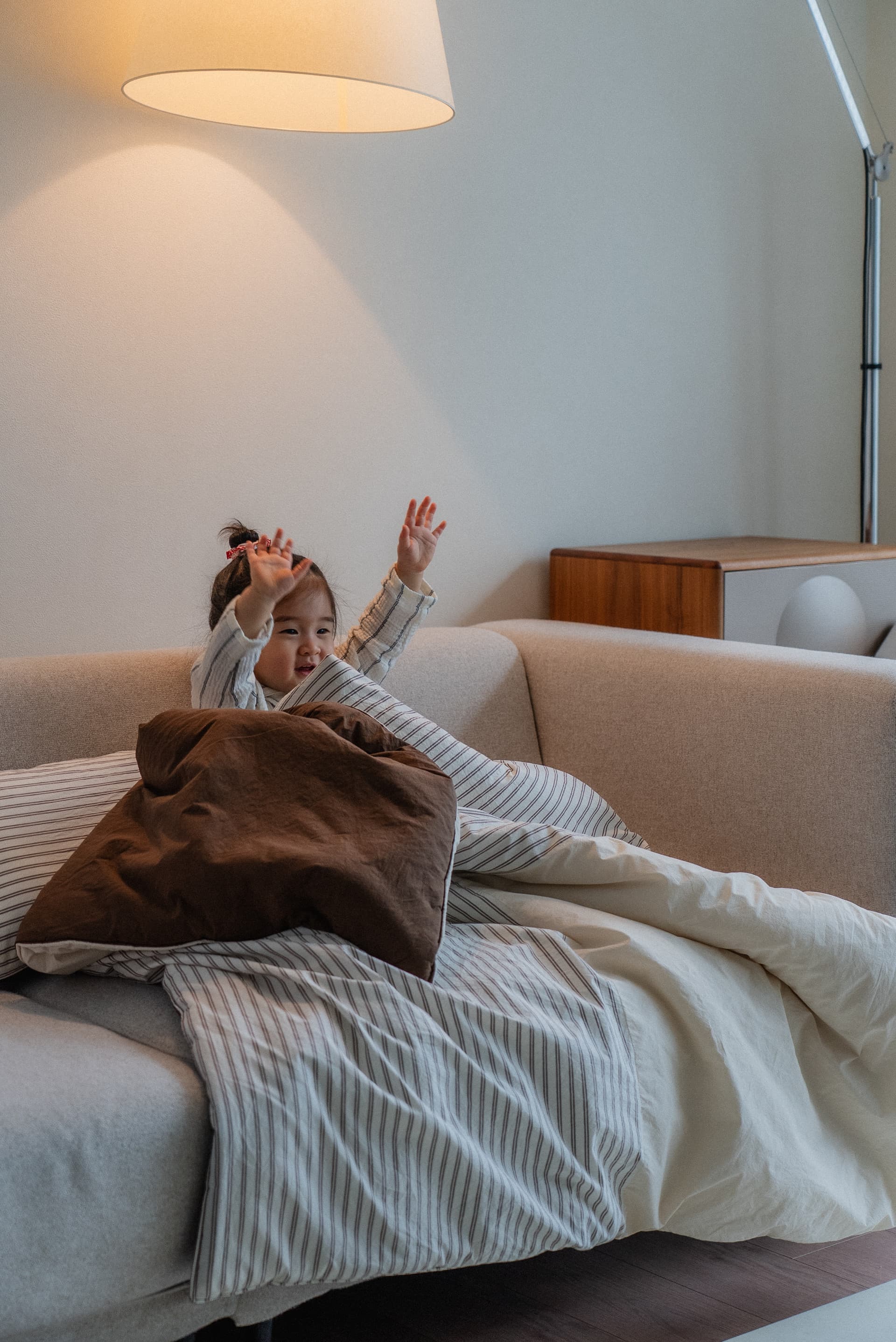 Joyful toddler playing on a sofa with our signature striped bedding